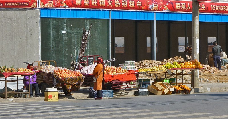 chinese ladies selling fruit while men rummage through garbage